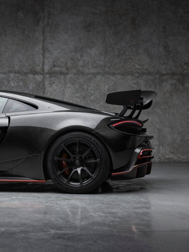 Dramatic studio lighting on the sharp carbon fiber rear wing of a modern hypercar, dark concrete background, minimal reflections