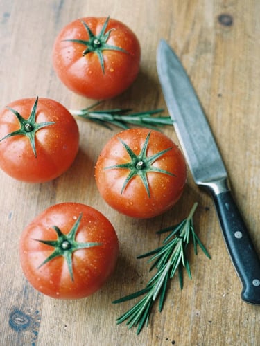 Overhead flat-lay of fresh heirloom tomatoes, rosemary sprigs, and a vintage chef knife on a rustic wooden table, soft natural daylight, shallow depth of field, 35mm film.