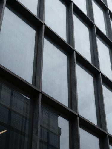 Tight abstract crop of a high-contrast architectural glass facade, cool slate tones, overcast light, sharp geometric angles with generous negative space.