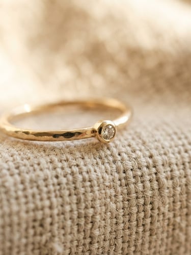 Macro photograph of a delicate gold ring resting on textured linen, soft warm morning light, shallow depth of field