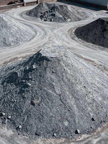 High-angle shot of raw mineral stockpiles in an organized industrial yard, cool desaturated tones, high contrast, 35mm lens.