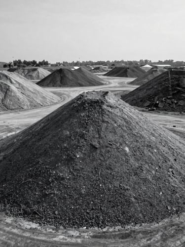High-angle shot of industrial mineral stockpiles in an open-air yard, overcast daylight, desaturated cool tones, high contrast, crisp details, 35mm lens