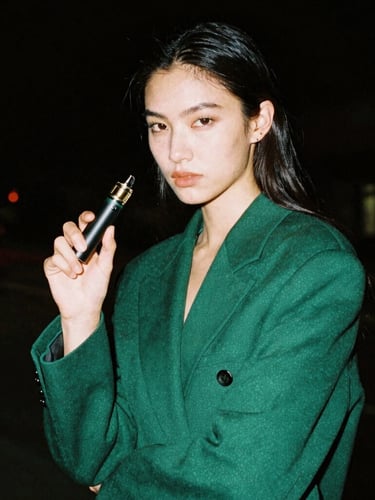 High-fashion lifestyle portrait of a confident model holding a sleek vape pen, low-key nocturnal lighting, dark tones, cinematic 35mm film.