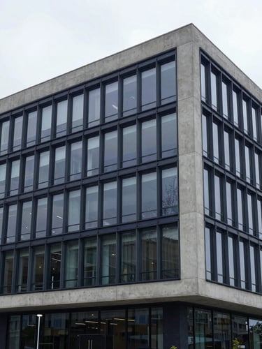 Wide architectural perspective of a modern, organized concrete and glass office building, cool bright overcast daylight, minimalist lines, 35mm