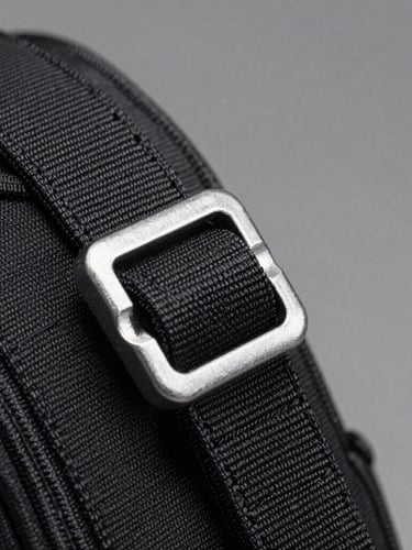 Crisp macro detail of heavy-duty tactical nylon stitching and steel buckle under harsh white studio spotlight, high contrast, neutral gray background, 50mm lens