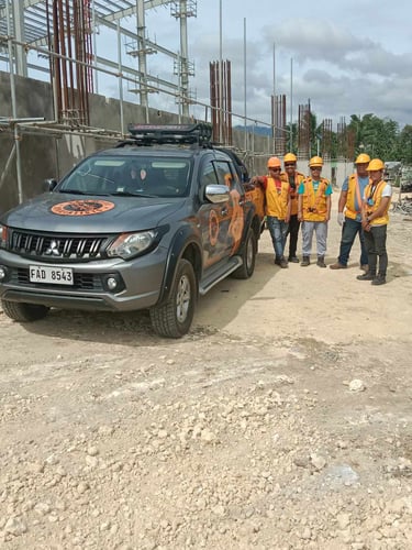 Construction workers in safety gear stand by a Mitsubishi pickup truck at a building site.