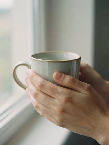 Close-up of hands holding a warm ceramic mug in soft morning window light, shallow depth of field, 35mm film look