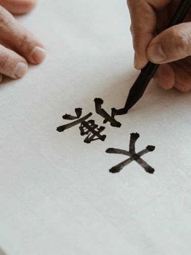 Close-up of hands writing Chinese calligraphy on handmade grid paper, the black ink slightly bleeding into the soft texture, warm indoor lamplight, quiet editorial composition.