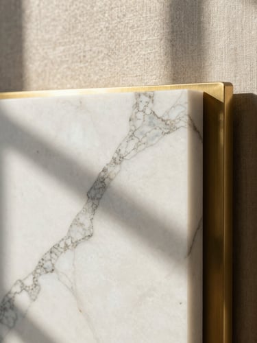 Close-up of premium materials, heavily veined white marble resting against textured raw linen and brushed brass accents, soft side window shadows, architectural digest style.