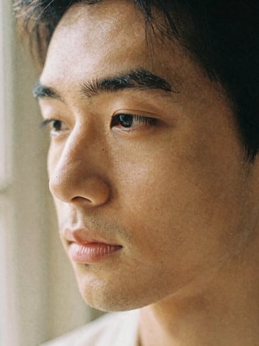 Close-up portrait of an individual under soft, diffused window light, showing natural skin texture and a calm expression, warm sand tones