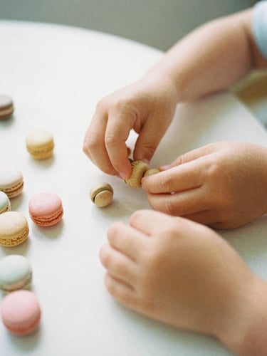 Eye-level candid photograph of a child's hands sorting smooth wooden beads on a sunlit table, soft morning daylight, gentle macaron pastel tones, shallow depth of field, 35mm film style