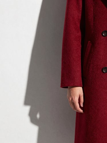 Architectural shadows cast on a structured deep crimson wool coat sleeve, high-contrast natural light, crisp parchment background, editorial fashion crop