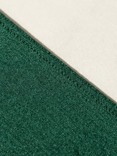 Macro detail shot of a heavy double-faced wool seam in matte forest green, high-contrast natural light, sharp directional shadows.