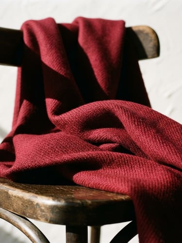 Close-up of structured heavy-weight crimson wool fabric draped elegantly over a studio chair, sharp directional shadows, crisp parchment background, 35mm lens