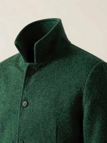 A close-up editorial shot of a heavy matte forest green wool collar and shoulder seam, high-contrast directional light, crisp parchment background, 35mm lens