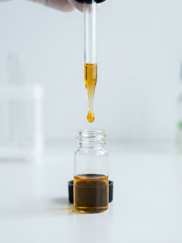 Macro photograph of a clear glass pipette with golden CBD oil dripping into a sterile laboratory vial, bright cool daylight, clinical white background, 50mm