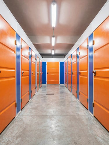 Brightly lit storage corridor with spotless concrete floors, rows of clean orange and navy storage unit doors under bright overhead LED lighting, sharp perspective lines.