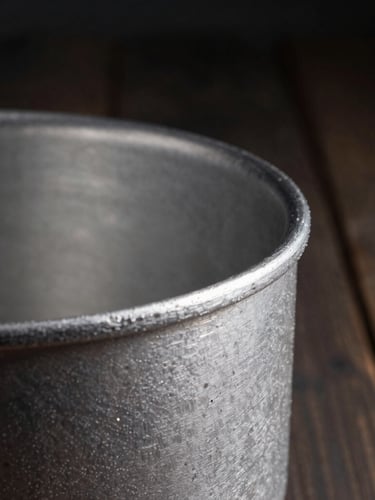 Macro shot of a thick cast aluminum pot rim, showing raw textured metal grain and hand-polished edge, dramatic side lighting, rustic dark wood background.