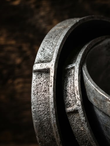 Close-up of thick cast aluminum pot rims with high-contrast side lighting, dramatic shadows highlighting metal textures, rustic dark background