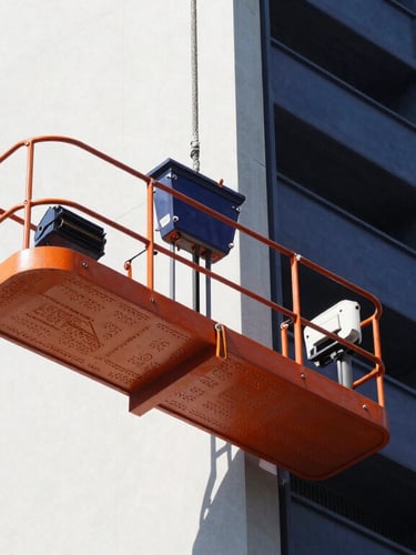A crisp industrial portrait of a modern rope suspended platform mounted on a clean high-rise facade under bright daylight, safety orange and navy blue details.