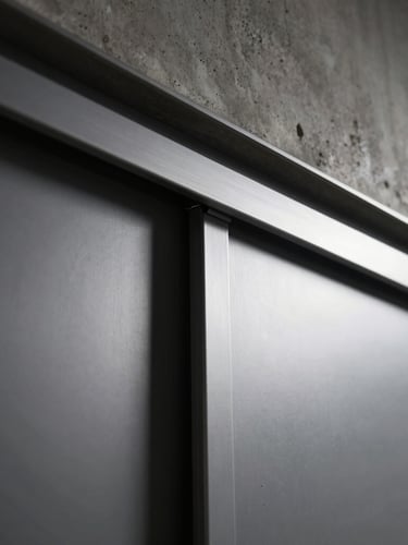 Tight architectural crop of a minimalist sliding door track installed in a raw concrete ceiling, hand sliding the heavy metal panel smoothly, deep shadows