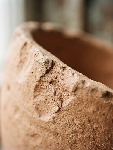 A tight macro shot of raw, unglazed terracotta clay edges, showing organic thumbprint texture under soft morning window light, shallow depth of field, 35mm