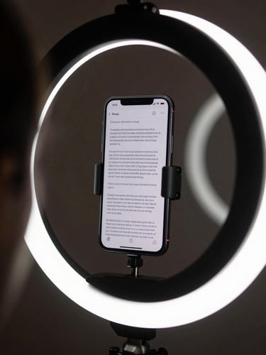 A close-up shot of a smartphone mounted on a ring light in a dimly lit room, displaying a highlighted script interface on screen, soft circular reflection in the background.