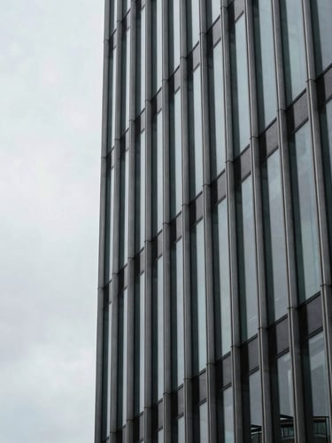 Tight architectural detail of a steel-and-glass curtain wall in the City of London, overcast sky, cool desaturated tones, sharp 35mm lens.