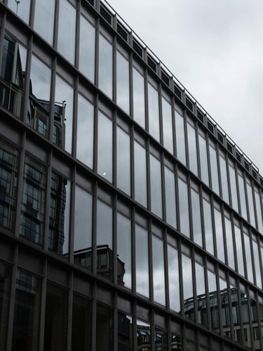 Steel-and-glass curtain wall of a City of London commercial building, reflecting overcast sky, high-contrast architectural geometry, deep shadows.