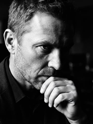 Extreme close-up, high-contrast black and white photography of a focused executive in deep shadow, hard directional side-lighting, sharp 35mm film grain, off-center composition