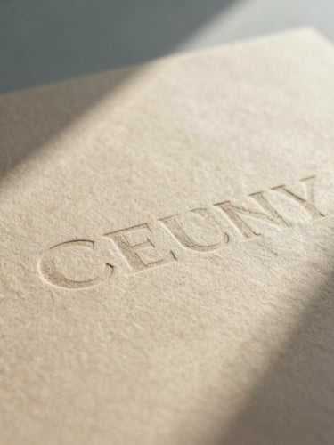 A close-up of tactile printed brand collateral on textured warm beige paper stock, soft natural shadows