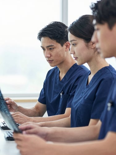 Medium close-up of three medical specialists in deep blue scrubs analyzing clinical scans on a monitor, soft natural window light, shallow depth of field