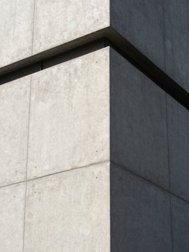 Sharp architectural angle of a modern concrete building facade, crisp daylight shadows, minimalist composition.