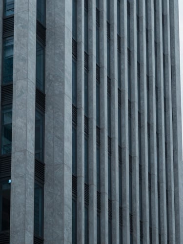 Editorial architectural photography of a modern financial district building facade with sharp geometric shadows, desaturated blue and slate tones, cool overcast daylight, 35mm lens