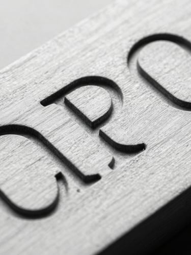 Extreme close-up of sharp, deeply engraved sans-serif typography on a pale maple wood surface, clinical studio lighting, harsh contrast.