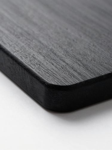Stark minimalist macro shot of a black engraved hard maple cutting board edge, sharp studio lighting, deep shadows, clinical white background