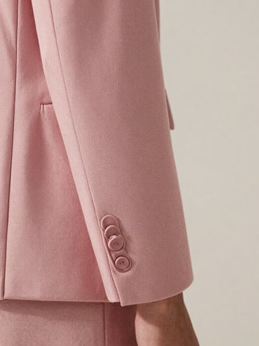 Close-up editorial photography of a beautifully tailored cuff and seam on a dusty pink structured jacket, soft natural daylight, minimalist background