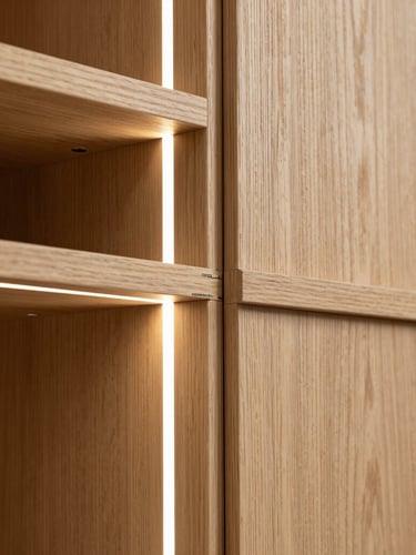 A close-up architectural shot of a bespoke oak wardrobe joint with integrated LED lighting, highlighting precise millimeter alignment and natural wood grain