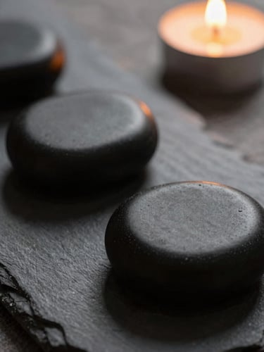 Close-up macro shot of warm, smooth black massage stones resting on raw grey linen, soft candlelight, moody shadows