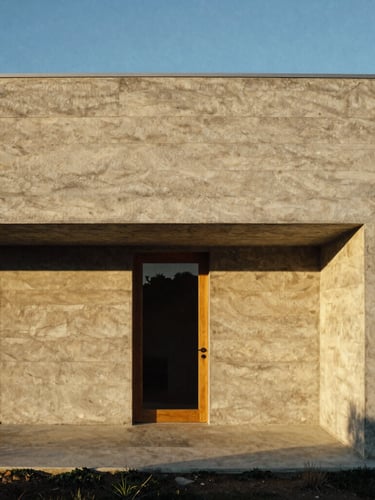Straight-on architectural elevation of a raw concrete and timber coastal home, sharp geometric shadows, low-angle golden hour light, warm travertine tones, 35mm film photography.