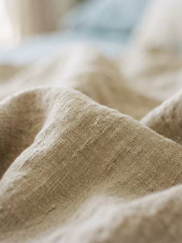 Close-up of soft organic linen fabric, warm sand tones, diffused morning daylight, gentle shadows, shallow depth of field, 35mm