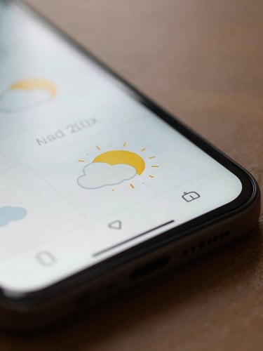 Macro close-up of a physical Android device displaying a minimalist weather utility, soft diffused afternoon workspace lighting, gentle shadows, focus on tactile screen details.