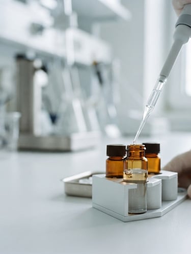 Macro close-up of amber glass vials filled with clear NAD+ solution, laboratory pipette dispensing liquid, bright cool daylight, minimalist clinical setting, sharp focus, high-end editorial, 35mm, with generous negative space to the left.
