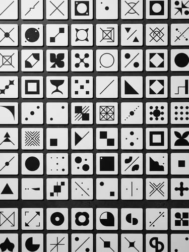 Overhead flat-lay of minimalist black and white game cards arranged in a perfect geometric grid on a dark surface, sharp studio shadows