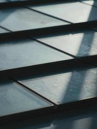 A close-up, high-contrast photograph of layered architectural glass sheets casting sharp, precise geometric shadows under cool, diffused daylight.