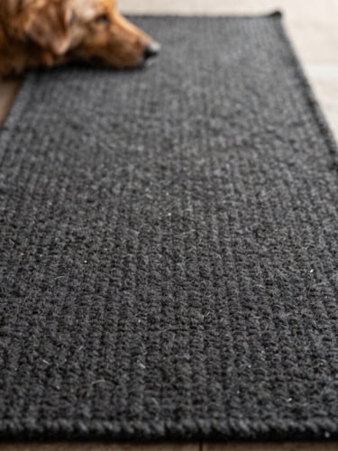 Floor-level close-up of a dog resting on a charcoal wool runner, soft afternoon light highlighting the thick tactile weave, shallow depth of field.