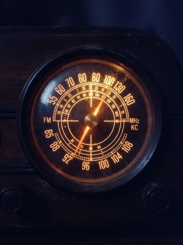 Extreme close-up of a vintage backlit radio dial glowing with warm marigold tungsten light, dust particles visible in the air, deep indigo shadows, 35mm film grain