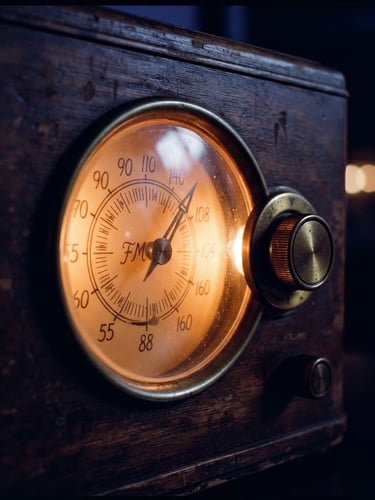 Close-up detail of a vintage wooden radio dial glowing with warm orange tungsten light, dark indigo background, moody low-key 35mm film style