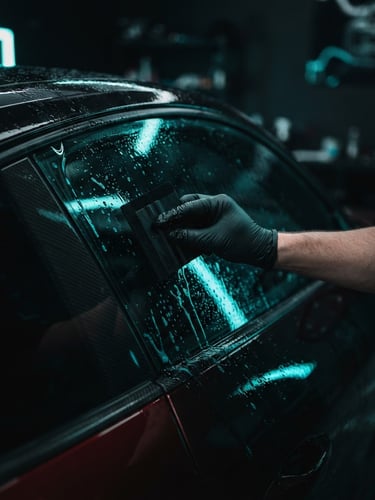 Moody automotive photography, close-up of a hand applying a dark nanoceramic window film to a sports car window, neon-cyan highlights reflecting off wet glass, 35mm.