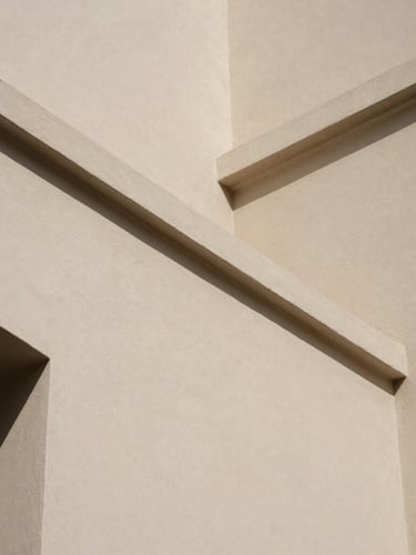 Close-up architectural detail of shadow lines on a smooth plaster wall, warm natural daylight, minimalist aesthetic, muted organic tones.